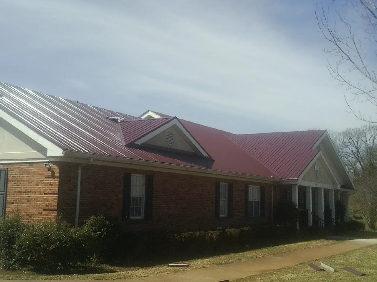 Red metal roof with gabled entries on a long brick building, from a Hail Damage Roof Repair job in Weirsdale