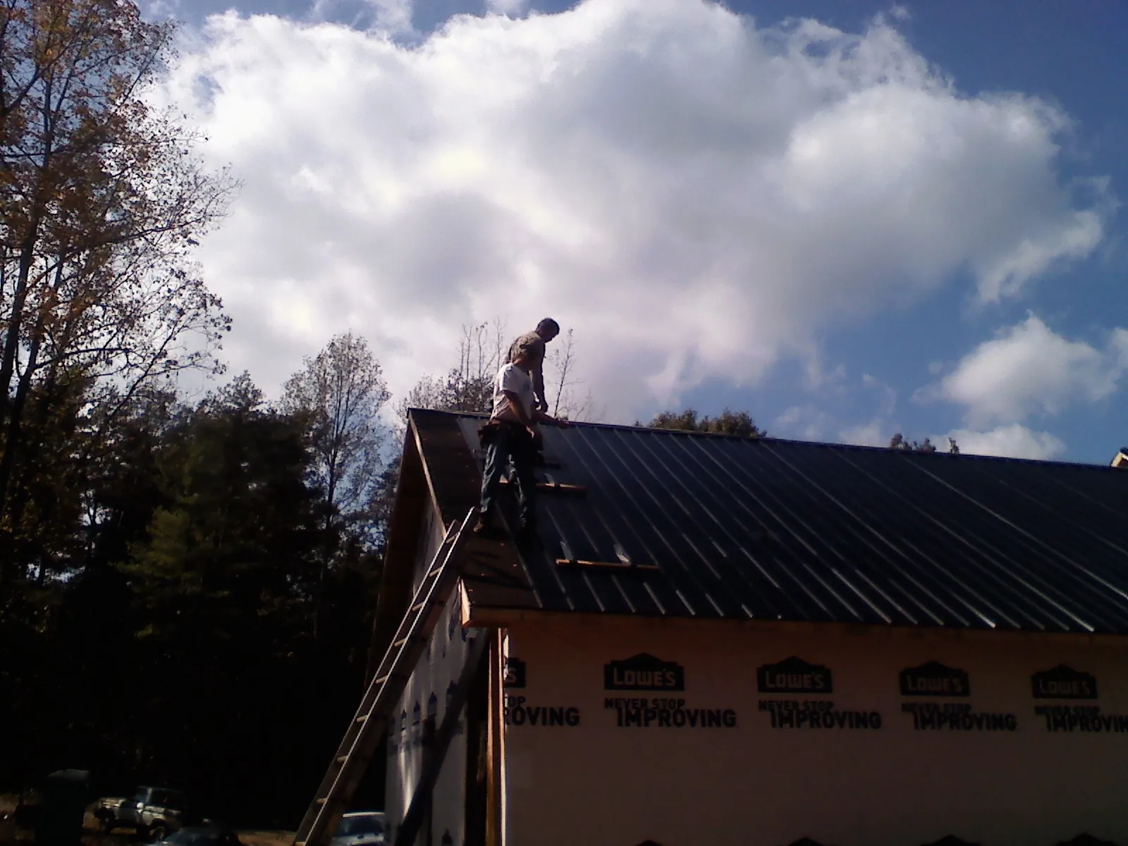 Roofer fastening dark metal panels high against a cloudy sky, from a Roof Inspection job in Weirsdale