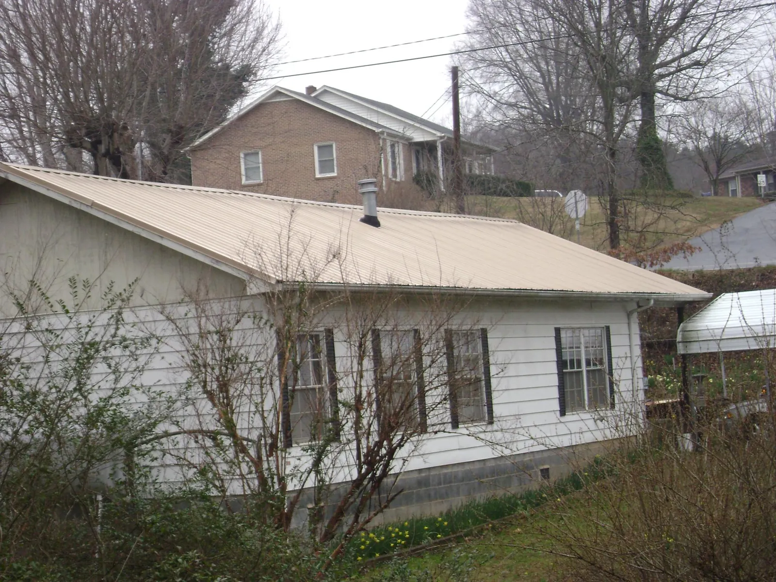 Tan metal roof on a white sided house set into a hillside — Commercial Roofing by Roofing Brothers in Weirsdale