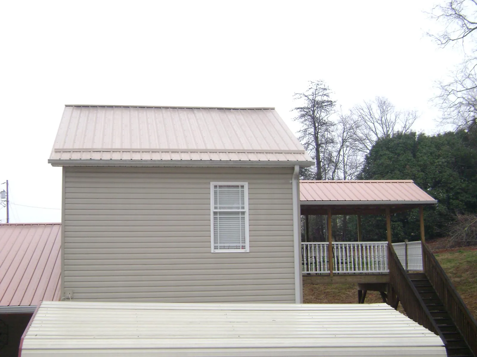 Tan metal roofs on a two story addition and attached porch, from a Roof Replacement job in Weirsdale